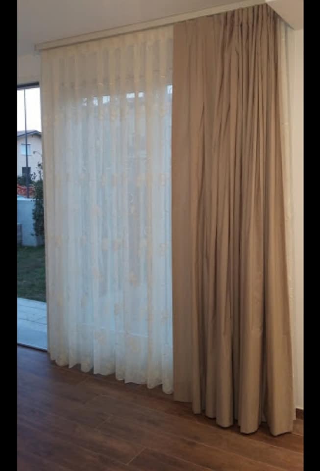 Tende trasparenti bianche e beige accanto a una porta a vetri su un pavimento in legno.