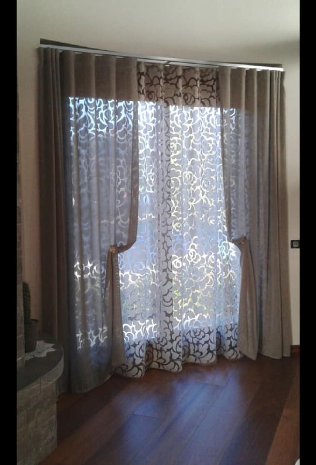 Tende floreali trasparenti su una finestra luminosa in una stanza con pavimento in legno