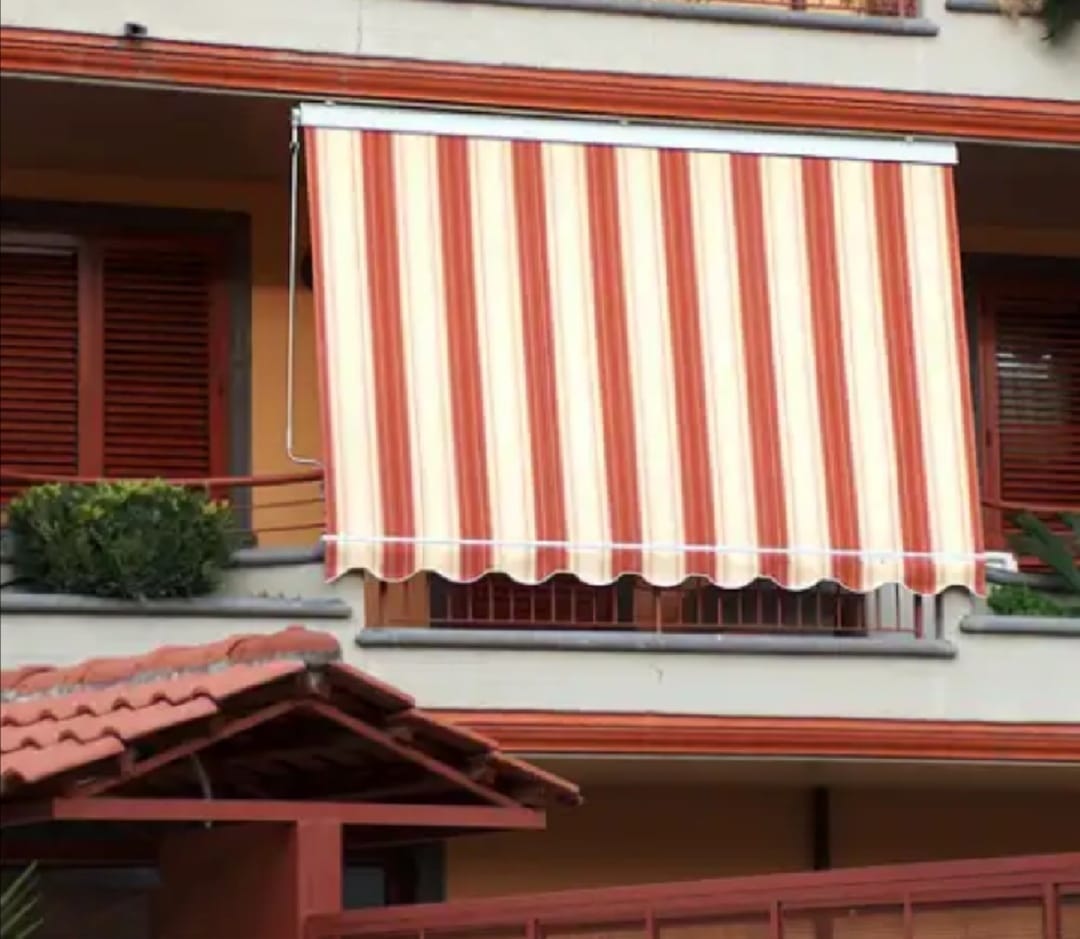 Tenda a righe rosse e bianche sopra una finestra sulla facciata beige di un edificio.