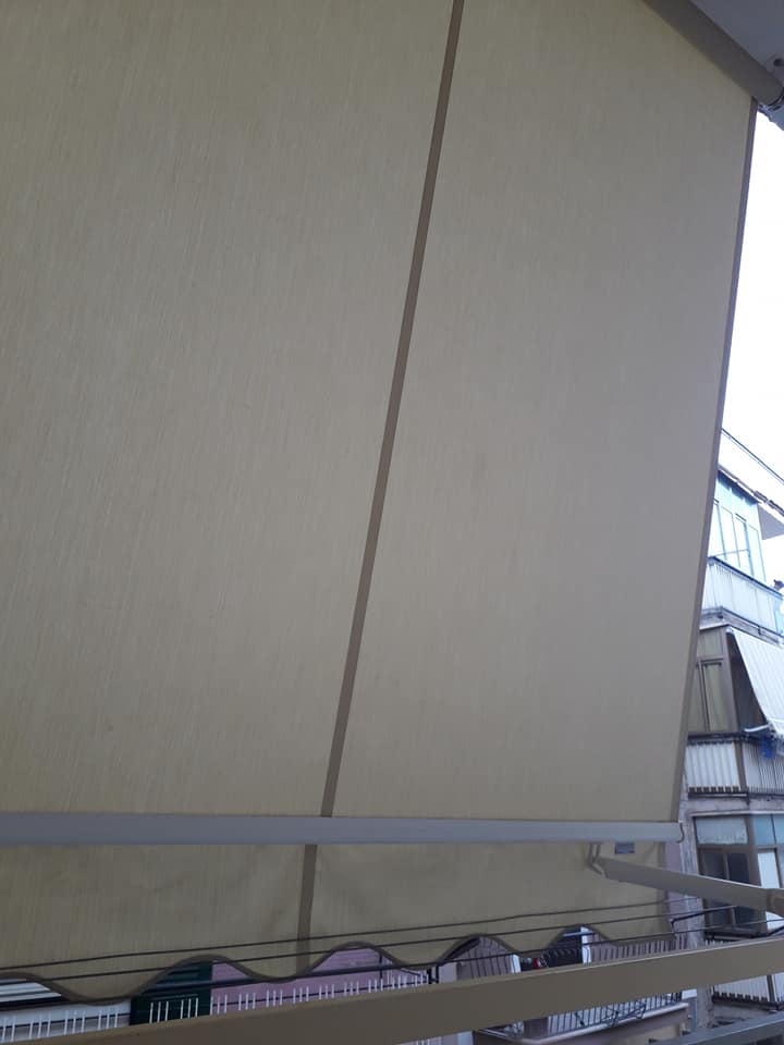 Muro di un edificio beige con giunture verticali e un condominio adiacente visibile sul lato destro.