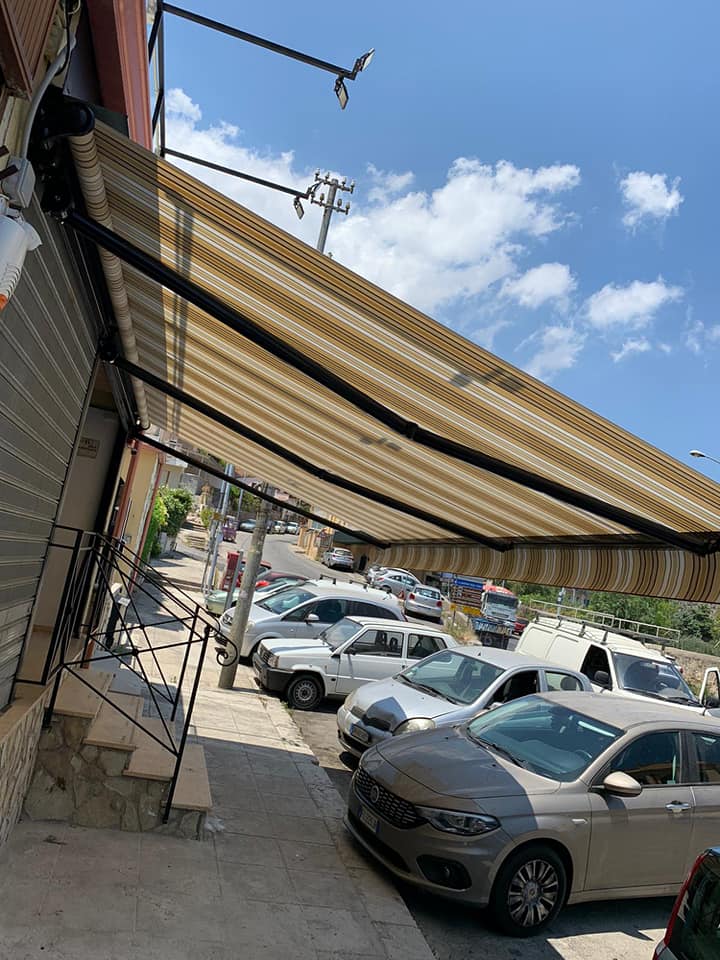 Parcheggio ombreggiato con diverse auto parcheggiate sotto tende a strisce, in una strada soleggiata.