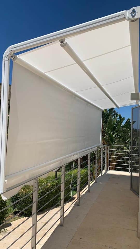 Balcone esterno con un'ampia tenda da sole retrattile bianca sopra una ringhiera e un passaggio pedonale.