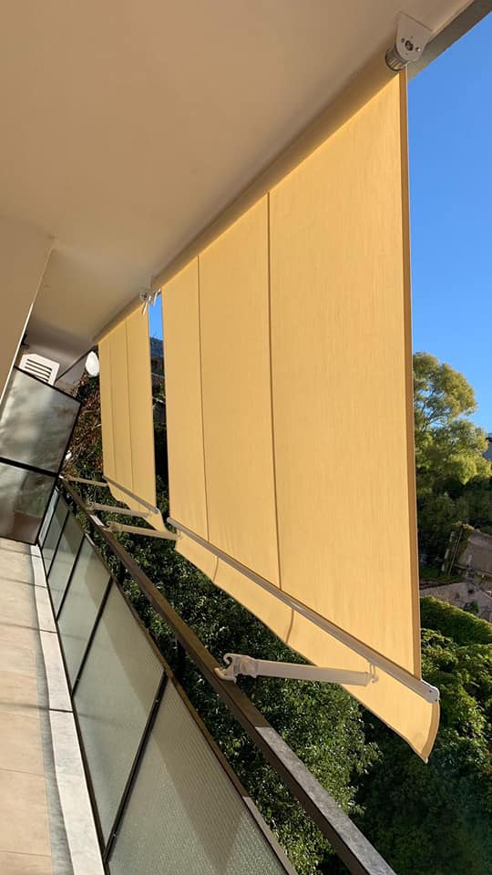 Balcone con tende parasole beige con vista sugli alberi e sul cielo azzurro.