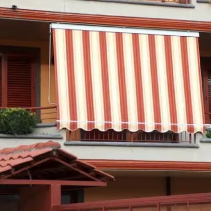 Tenda da sole a strisce arancioni e bianche sulla facciata color pesca di un condominio.