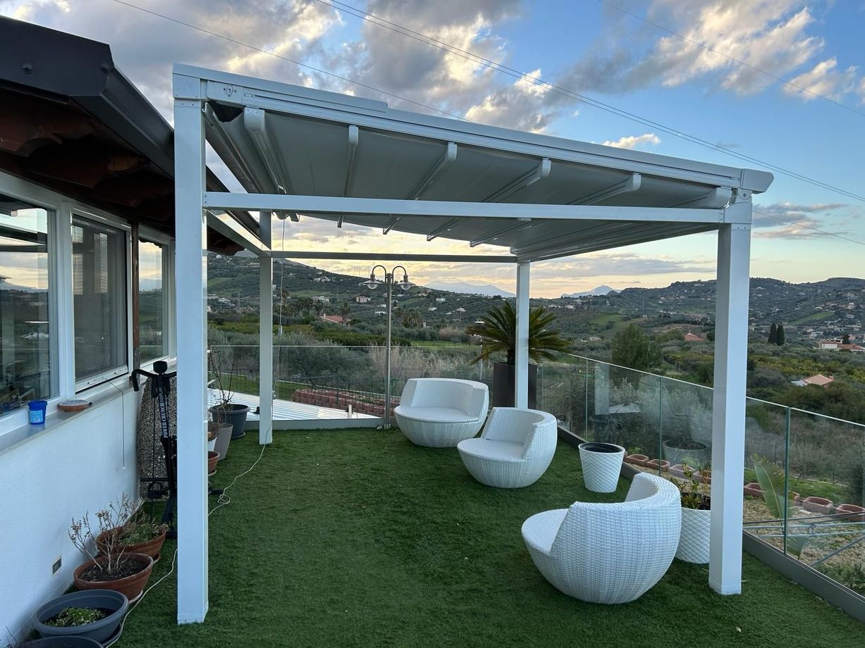 Patio moderno con pergola bianca, sedie imbottite e vista sulla collina al tramonto.