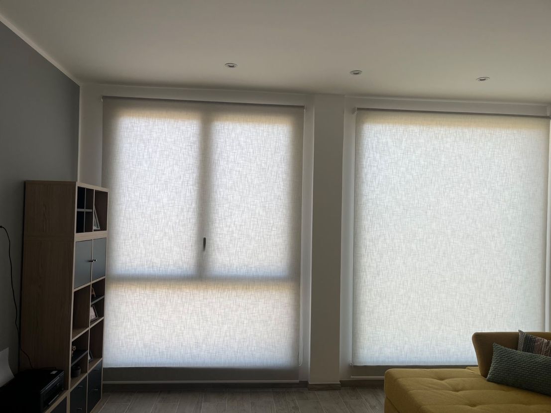Soggiorno minimalista con due grandi finestre coperte da tende bianche e una mensola in legno scuro.