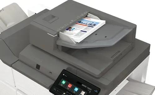 Multifunction printer, gray, with paper output tray containing printed pages. Touchscreen control panel.