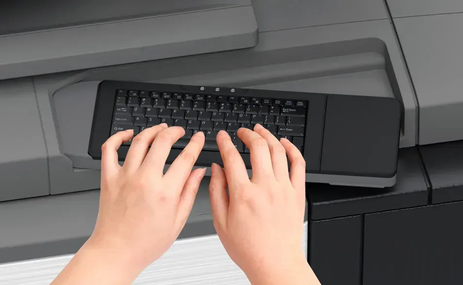 Hands typing on a small, black keyboard attached to a large printer.