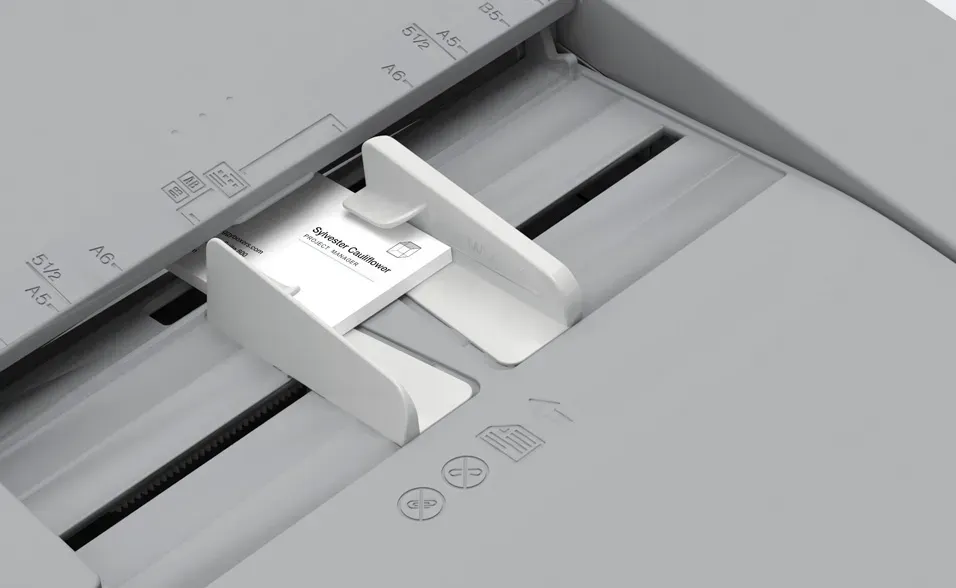 Business card in document feeder tray, positioned between white guides on a copier.
