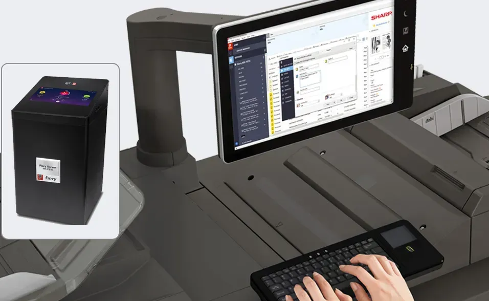Person using a keyboard at a large printer with a tablet showing software. A black box is inset to the left.