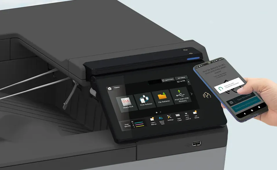 Hand holds phone near a printer screen; phone displays an app interface.