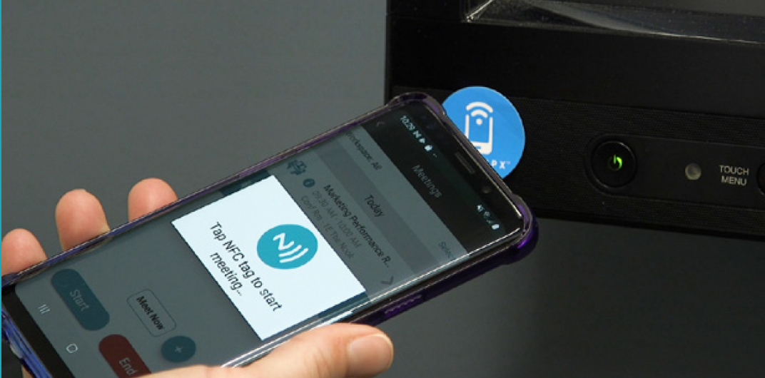 A hand holding a phone with a payment screen taps a device for contactless payment.