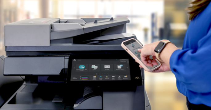 Woman using her smartphone to operate a printer in an office setting.