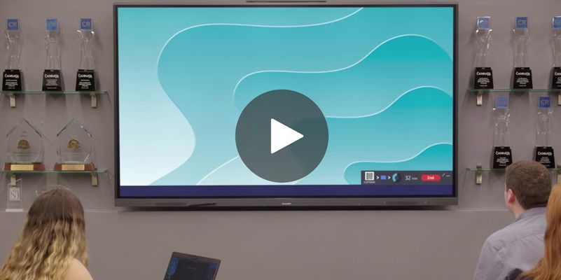 People watching presentation on a large screen with a play button. Awards line the wall.
