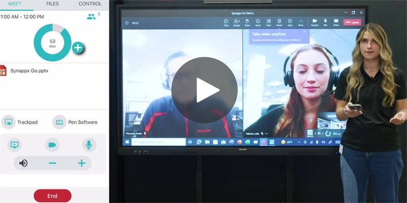 A woman is giving a presentation. A screen shows a video call. The woman is holding a remote.