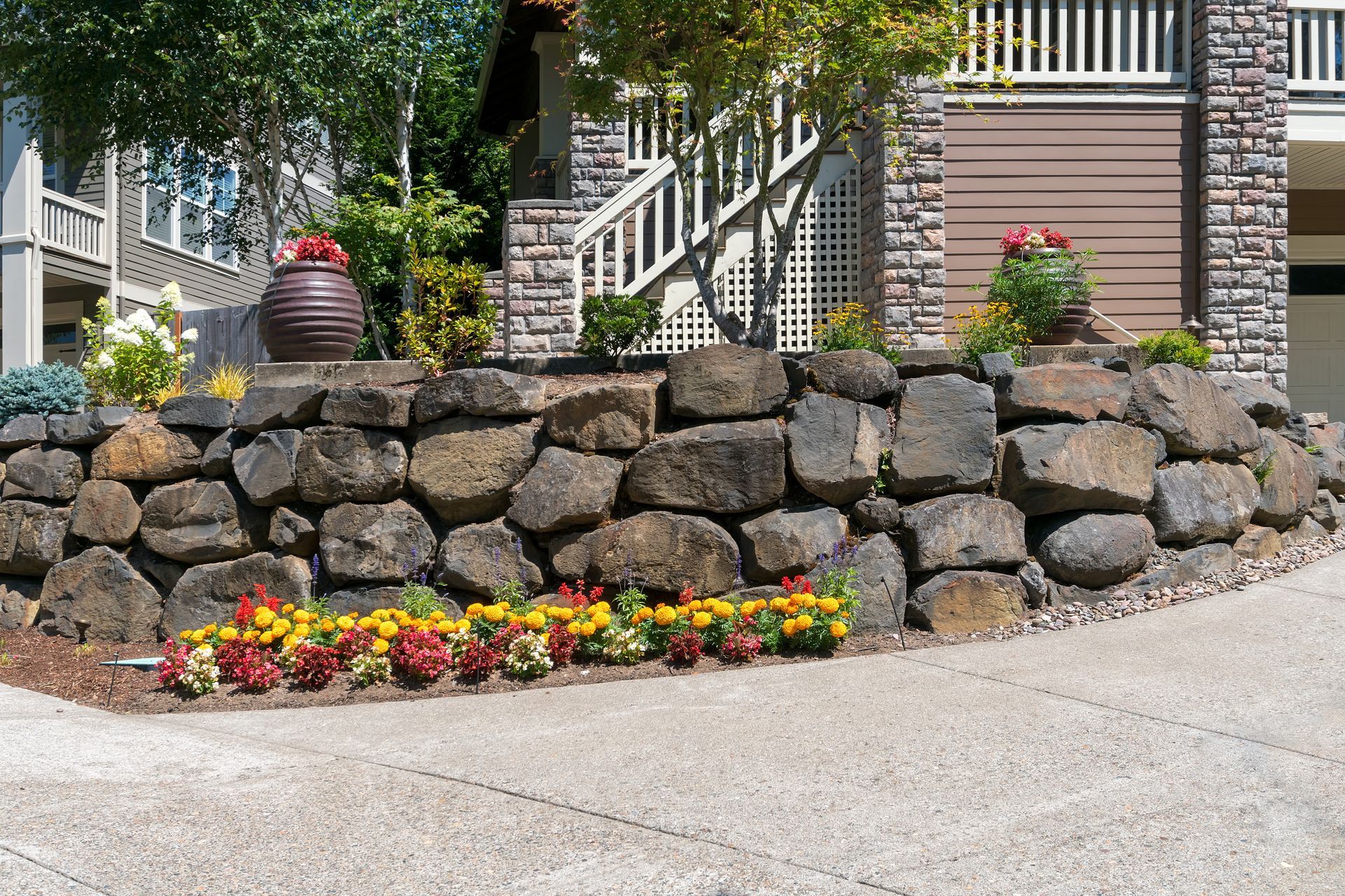 Stone retaining wall with colorful flowers along a garden path by a brick house.