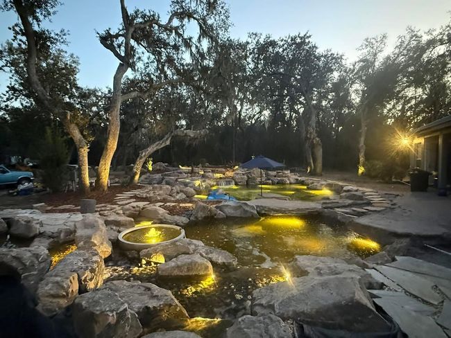 Outdoor stone garden with glowing yellow lights, trees, and a blue umbrella at dusk