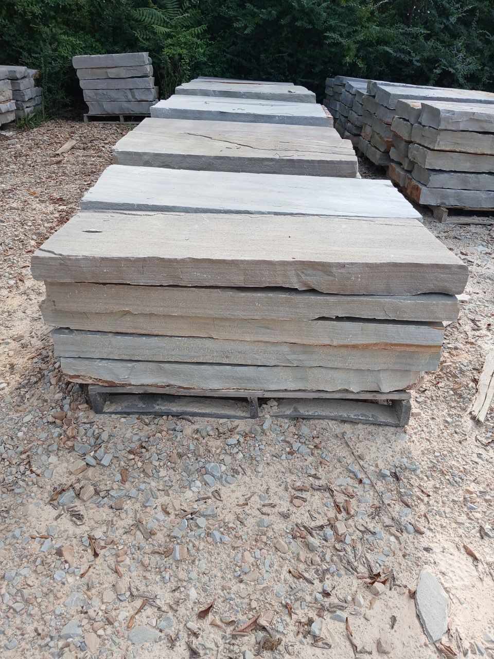Stacked gray stone slabs on gravel, with piles of stone on both sides outdoors