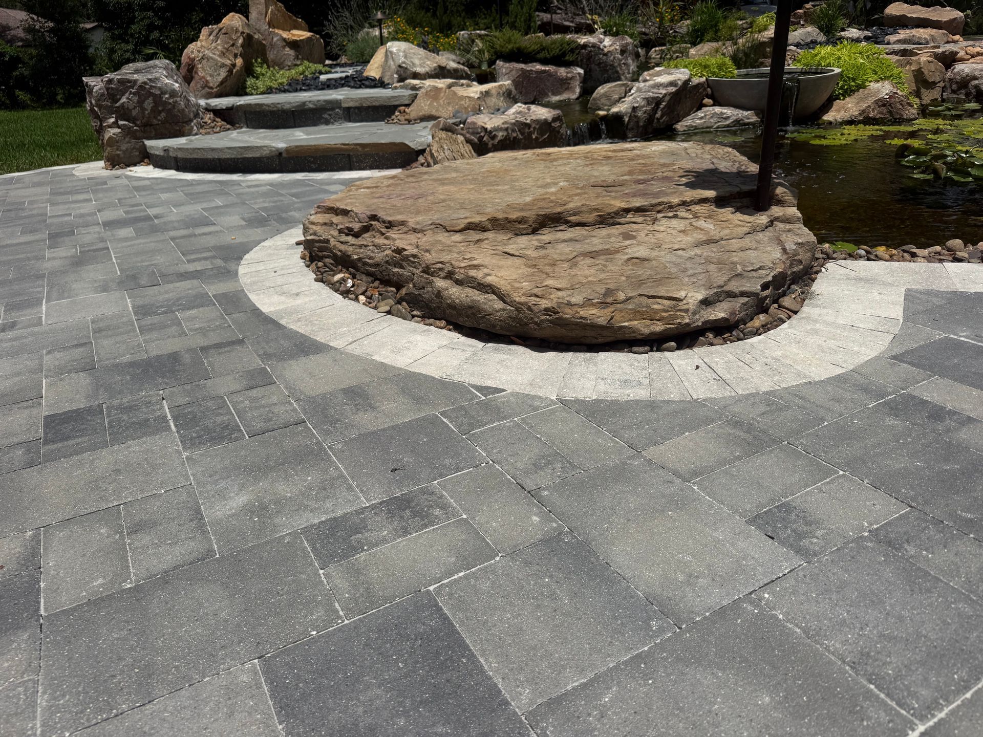 Stone patio with curved steps, rocks, and a landscaped garden area around a large boulder.