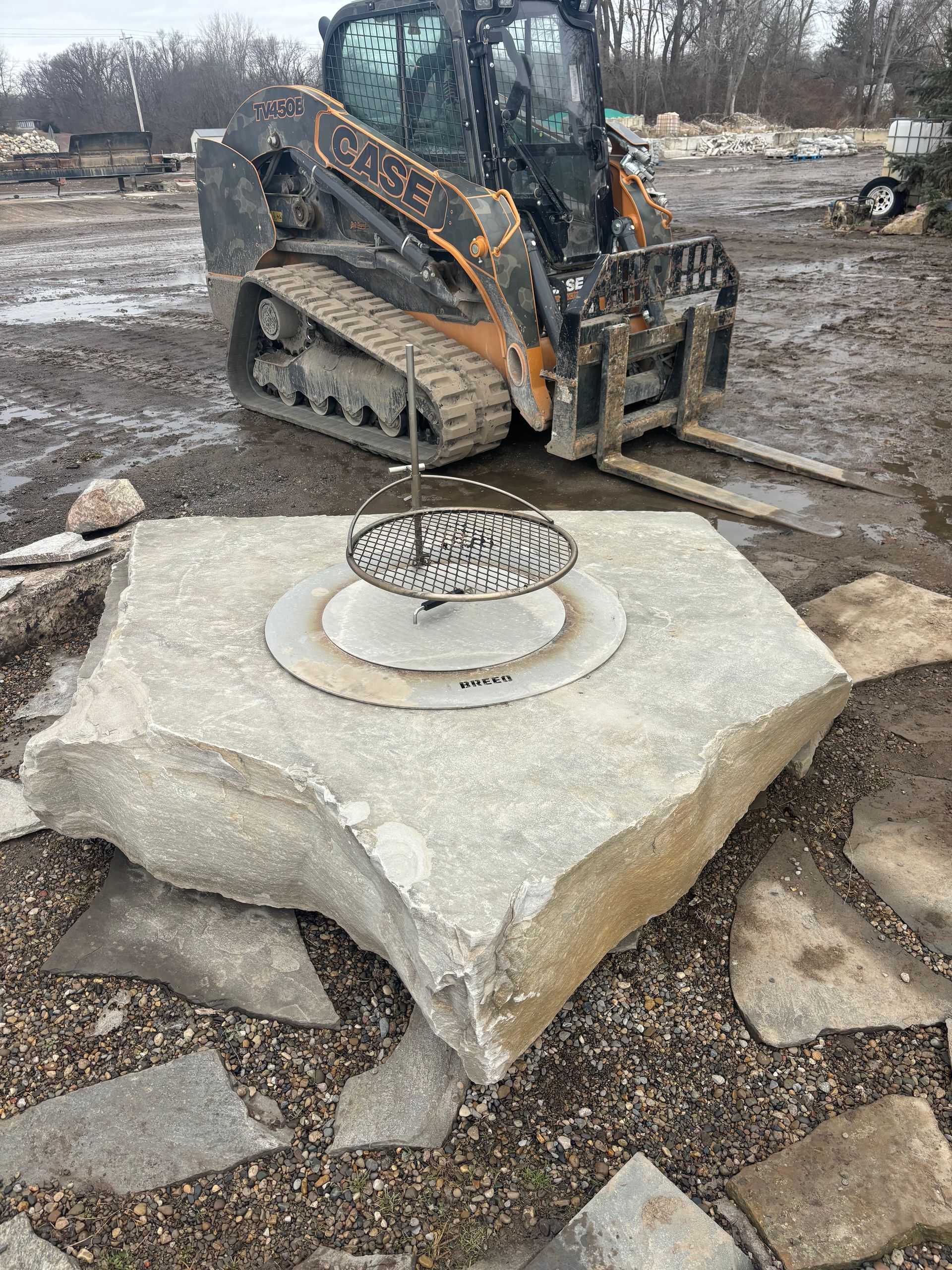 Skid steer near a large broken concrete slab with a circular metal frame in a muddy construction site