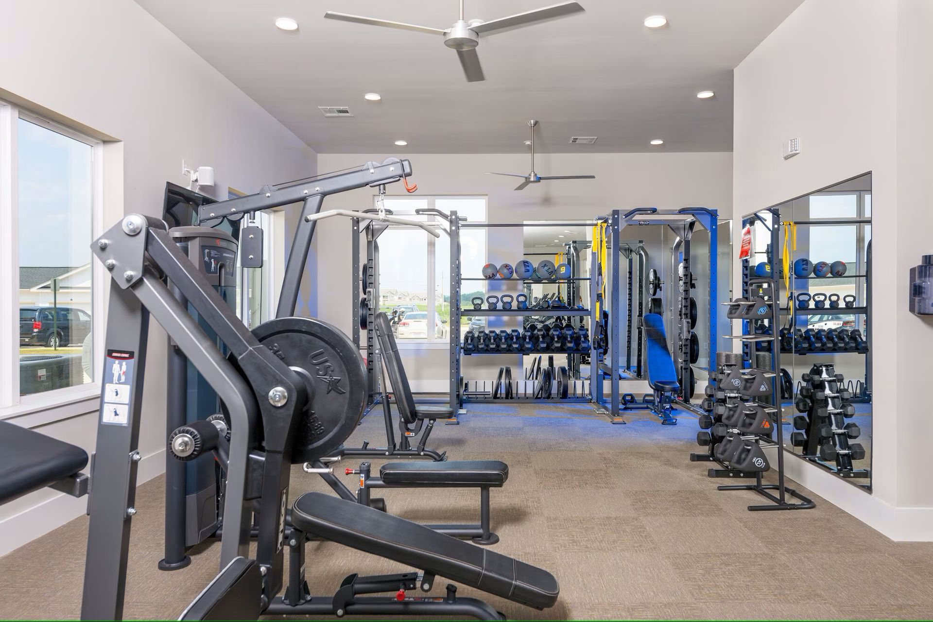 Gym with exercise machines, free weights, and mirrors. Interior view, neutral colors.