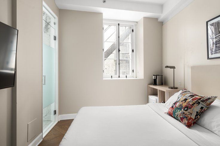Bedroom with a white bed, window, and a small desk area. A television is on the wall.