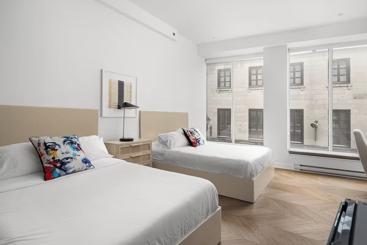 Two beds in a bright room with a city view.