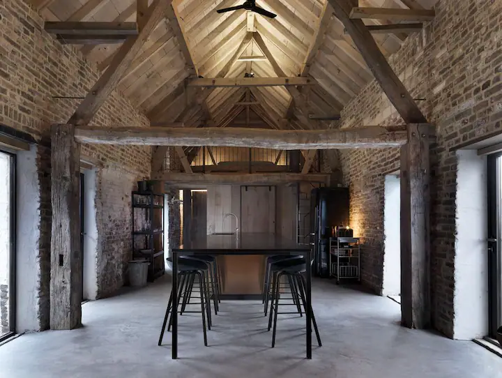 Interieur van ruimte met houten balken, betonnen vloer en een centrale zwarte bar met barkrukken.