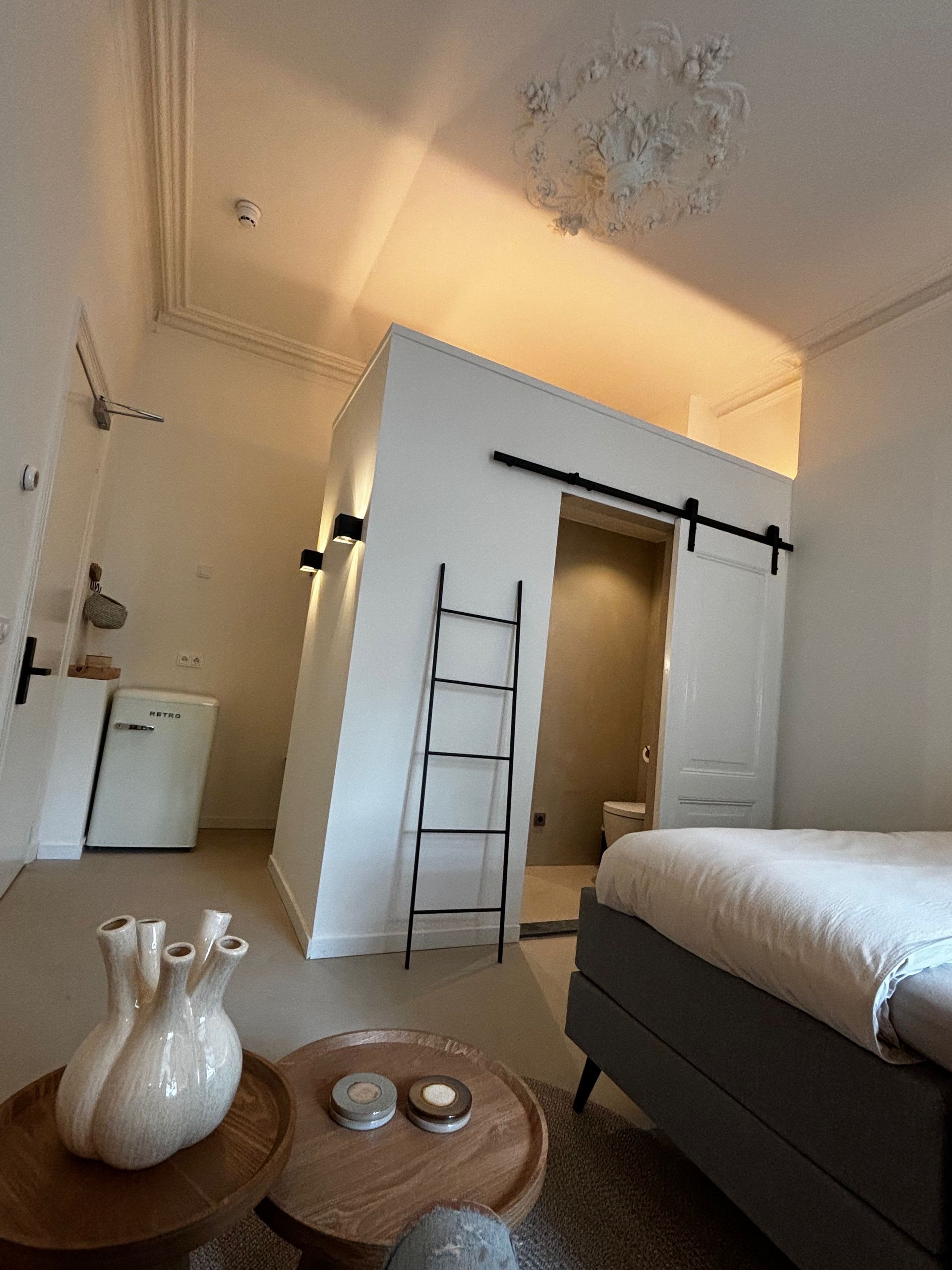 Moderne slaapkamer met een bed, een kleine keuken en een kleine badkamer die toegankelijk is via een schuifdeur.