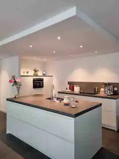 Moderne witte keuken met kookeiland, inbouwverlichting en ingebouwde oven.