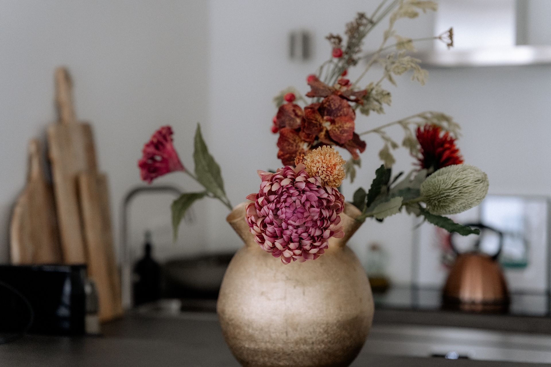 Een vaas met kleurrijke bloemen op het aanrecht; snijplanken en een gootsteen op de achtergrond.