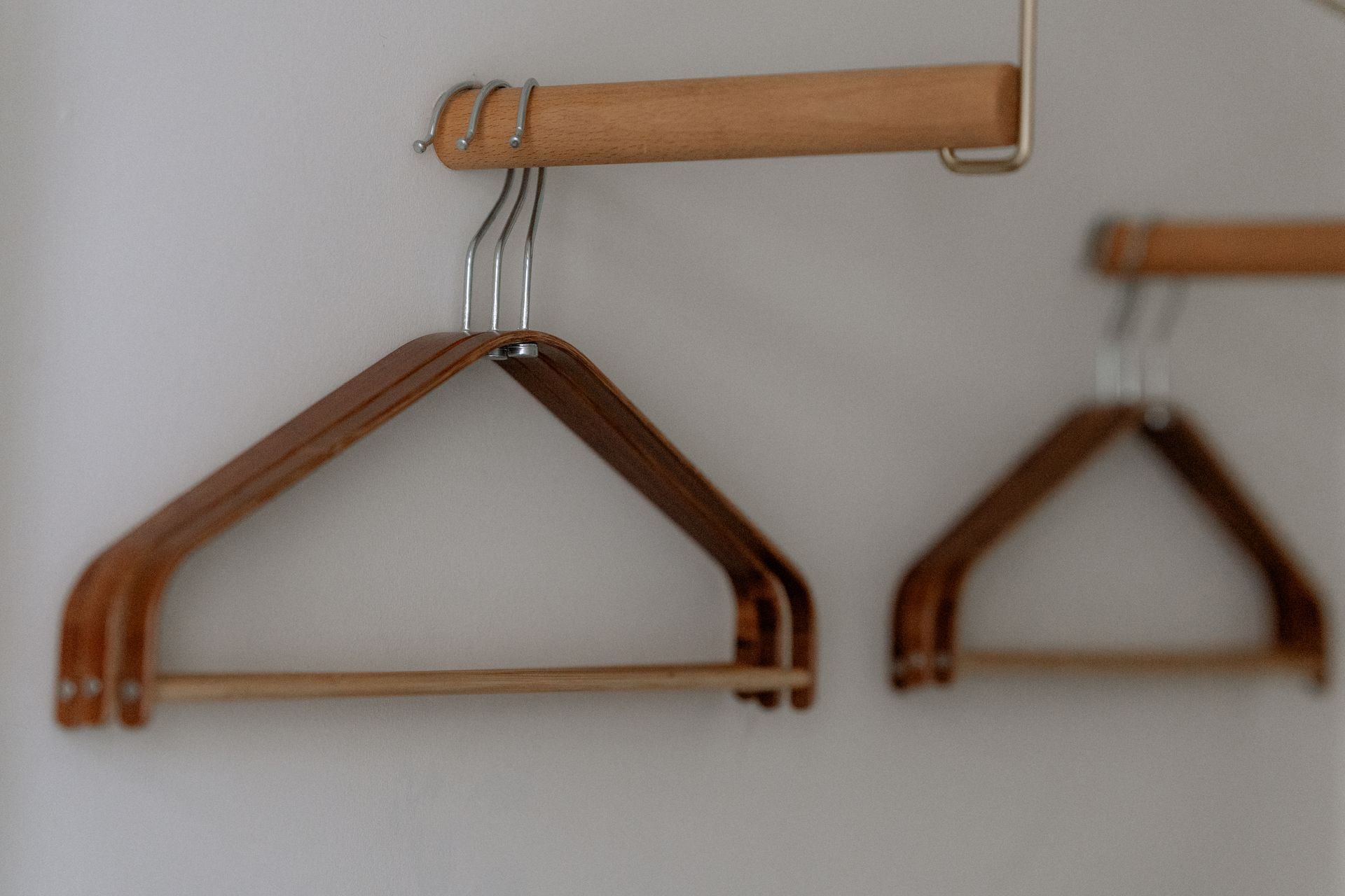 Houten kledinghangers hangen aan een houten stang tegen een witte muur.