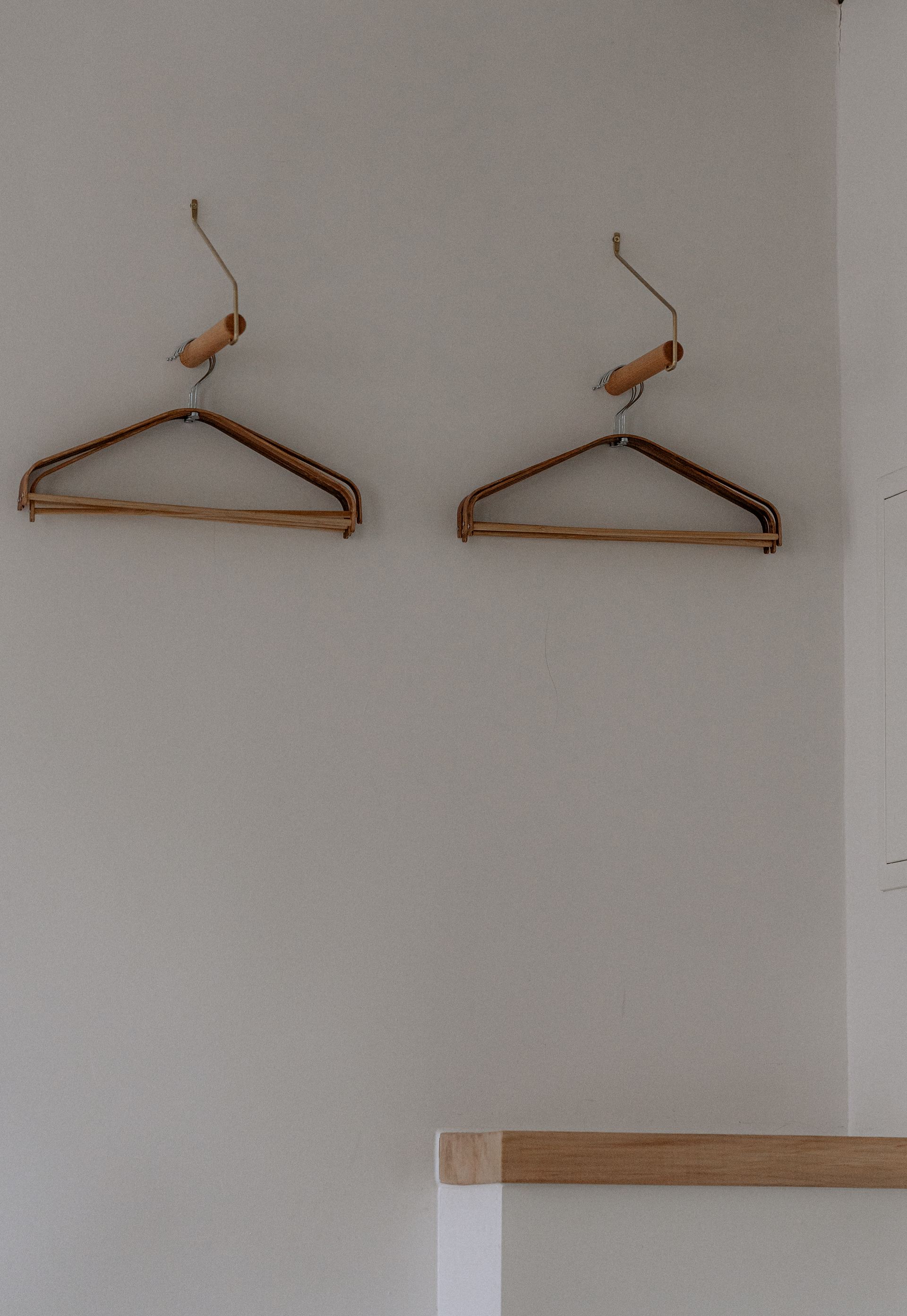 Aan een witte muur hangen twee houten kledinghangers.