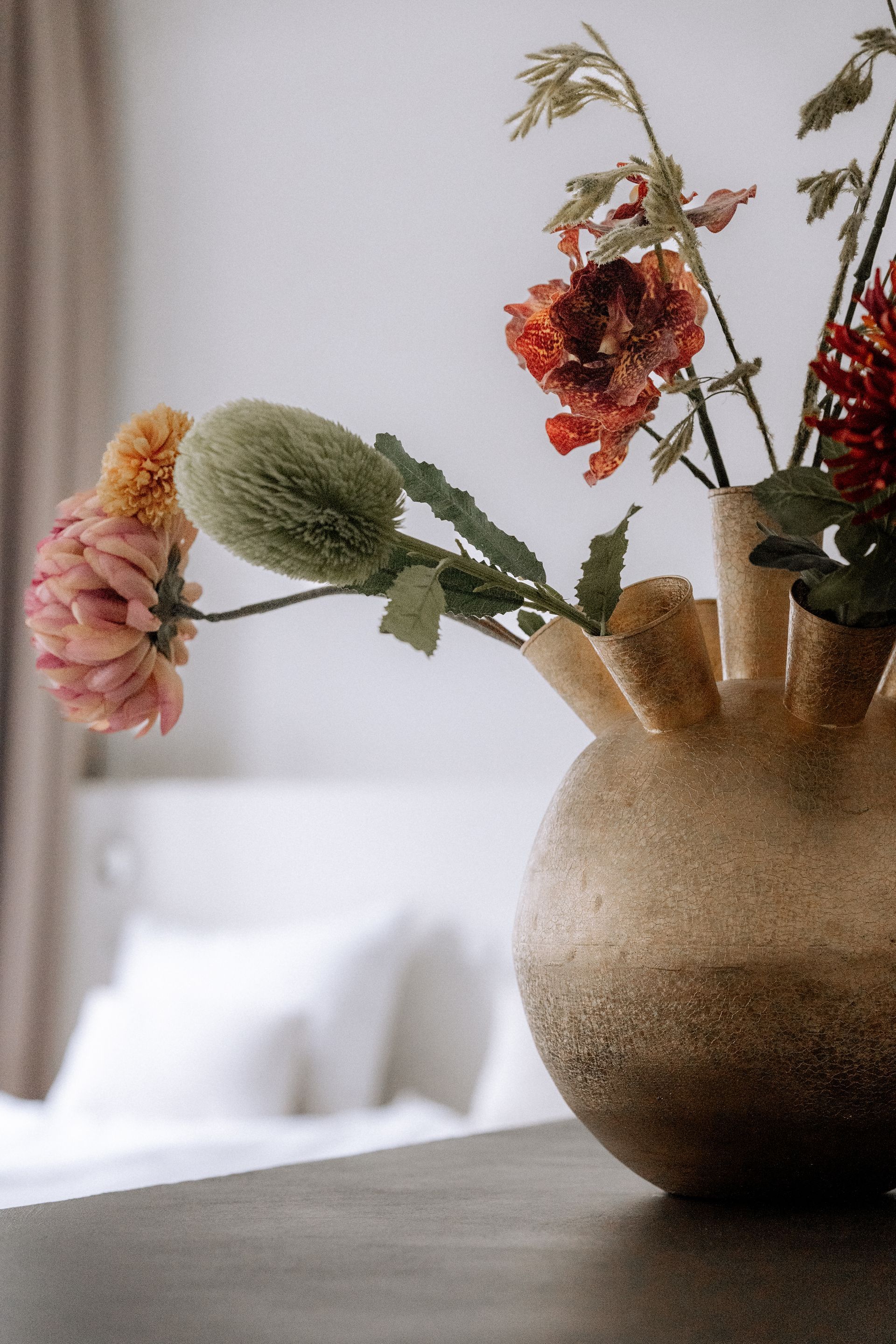 Gouden vaas met bloemen op een tafel. Roze, rode en groene bloemen met een wit bloembed op de achtergrond.