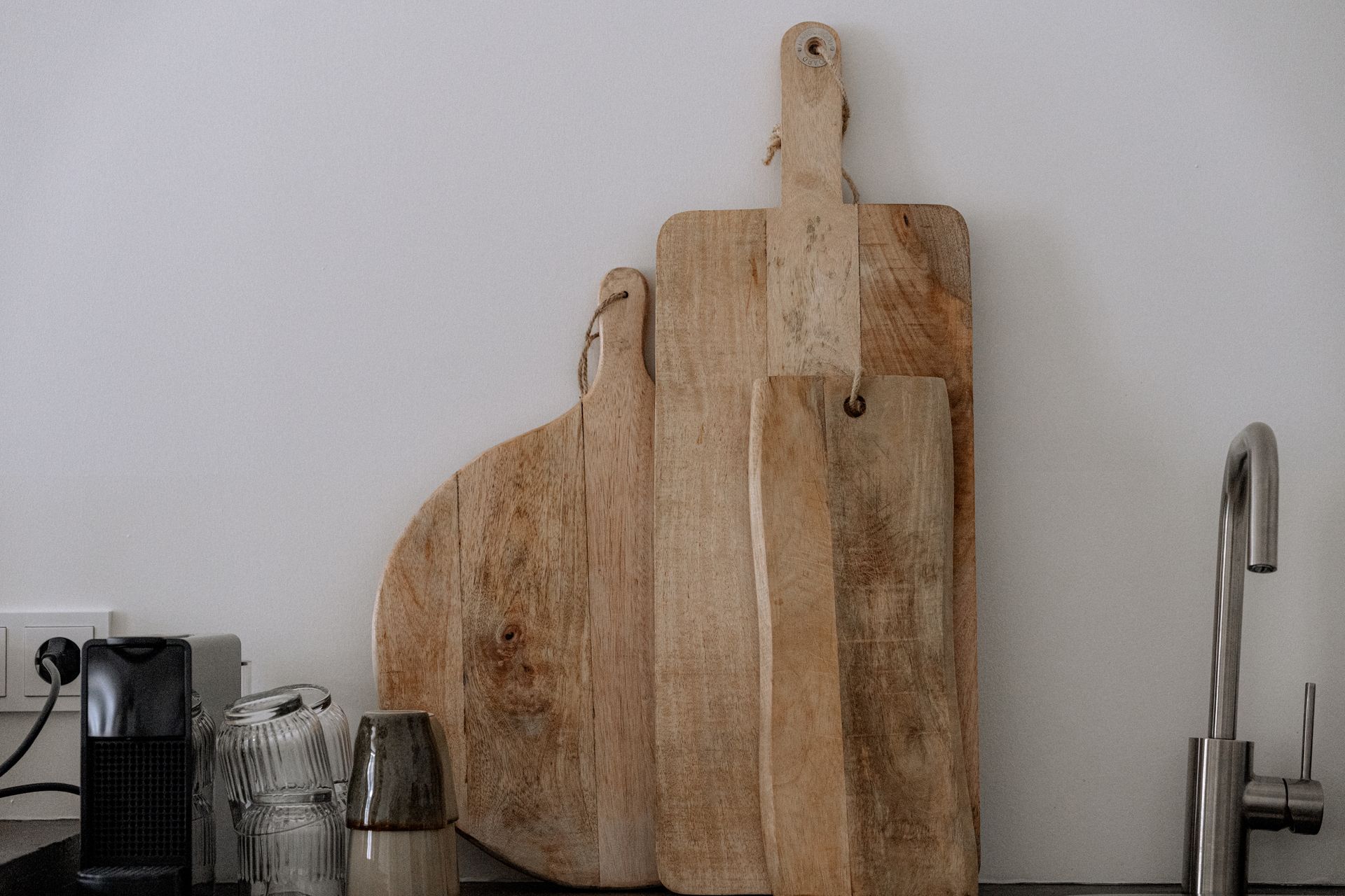 Drie houten snijplanken staan ​​tegen een witte muur, vlakbij een gootsteen en een koffiezetapparaat.