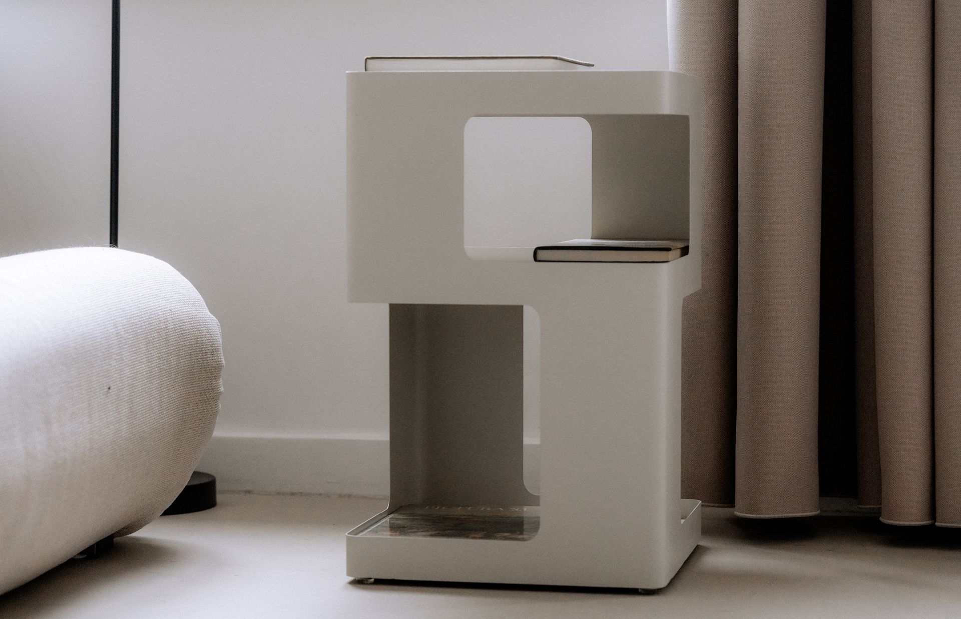 Witte, moderne bijzettafel met een vierkant ontwerp tegen een witte muur en gordijn.