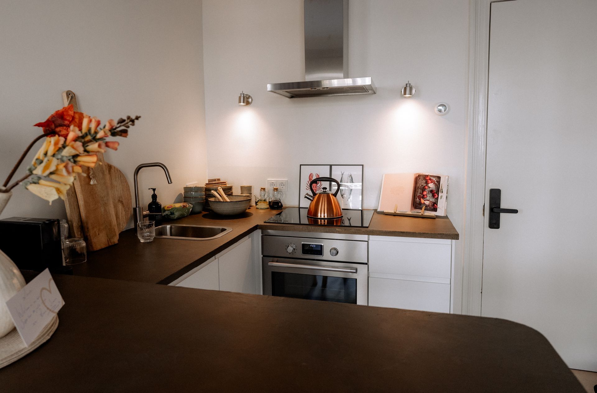 Kleine keuken met witte kasten, roestvrijstalen apparaten en bruine aanrechtbladen.
