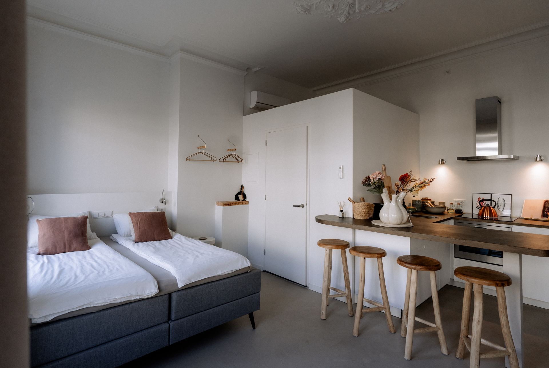 Studio-appartement met twee eenpersoonsbedden, een keukeneiland met barkrukken en witte muren.