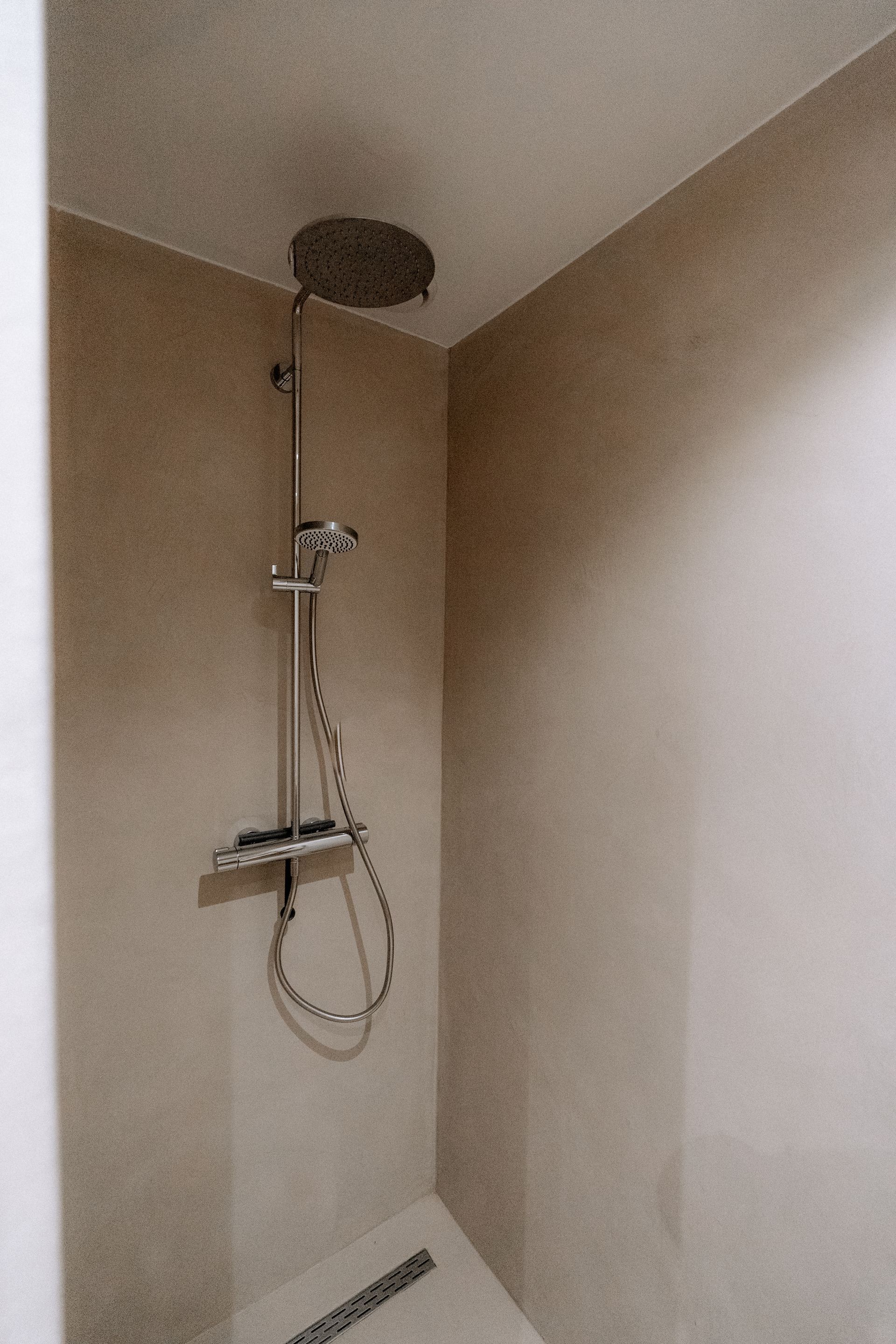 Douchecabine met regendouchekop en handdouche op een neutrale muur.