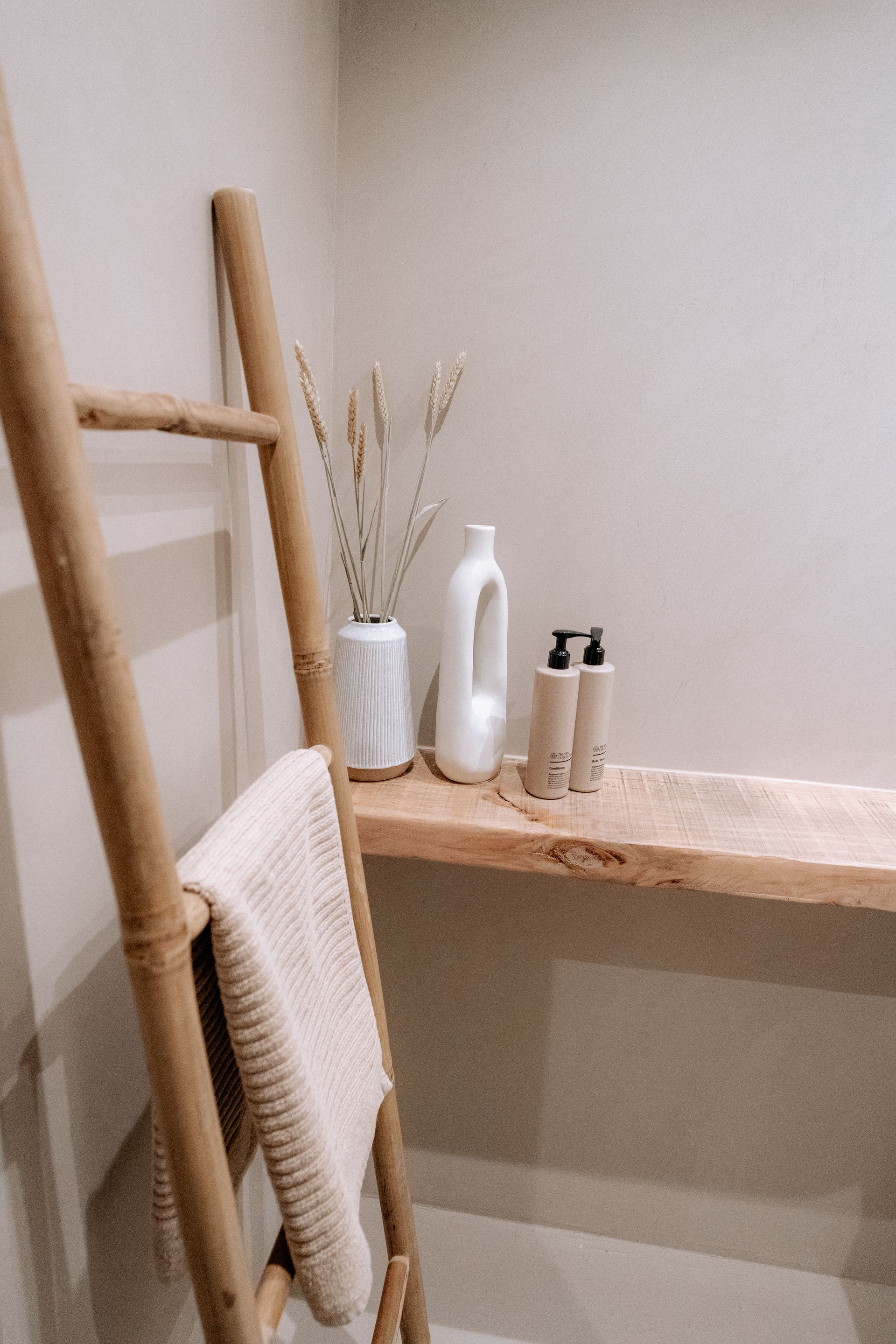 Houten ladder met handdoek naast een plank met decoraties in een badkamer in neutrale tinten.