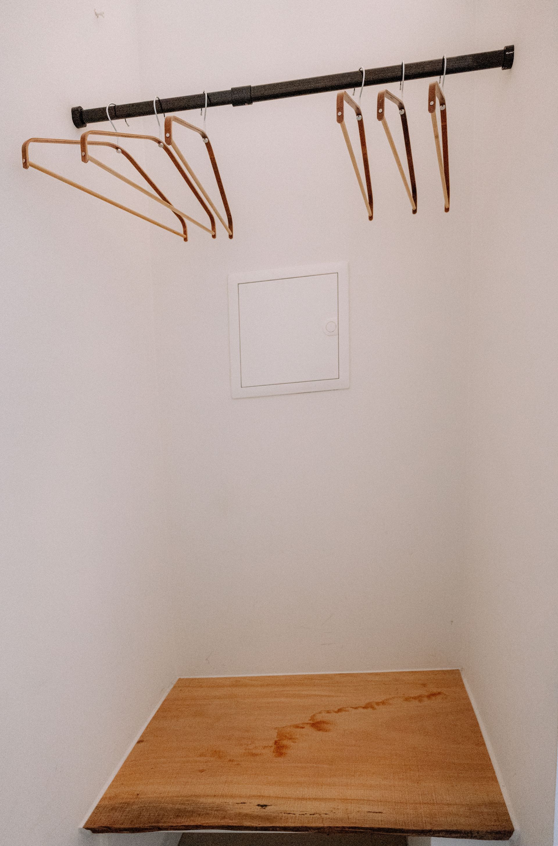 Lege kast met houten hangers, een plank en witte muren.