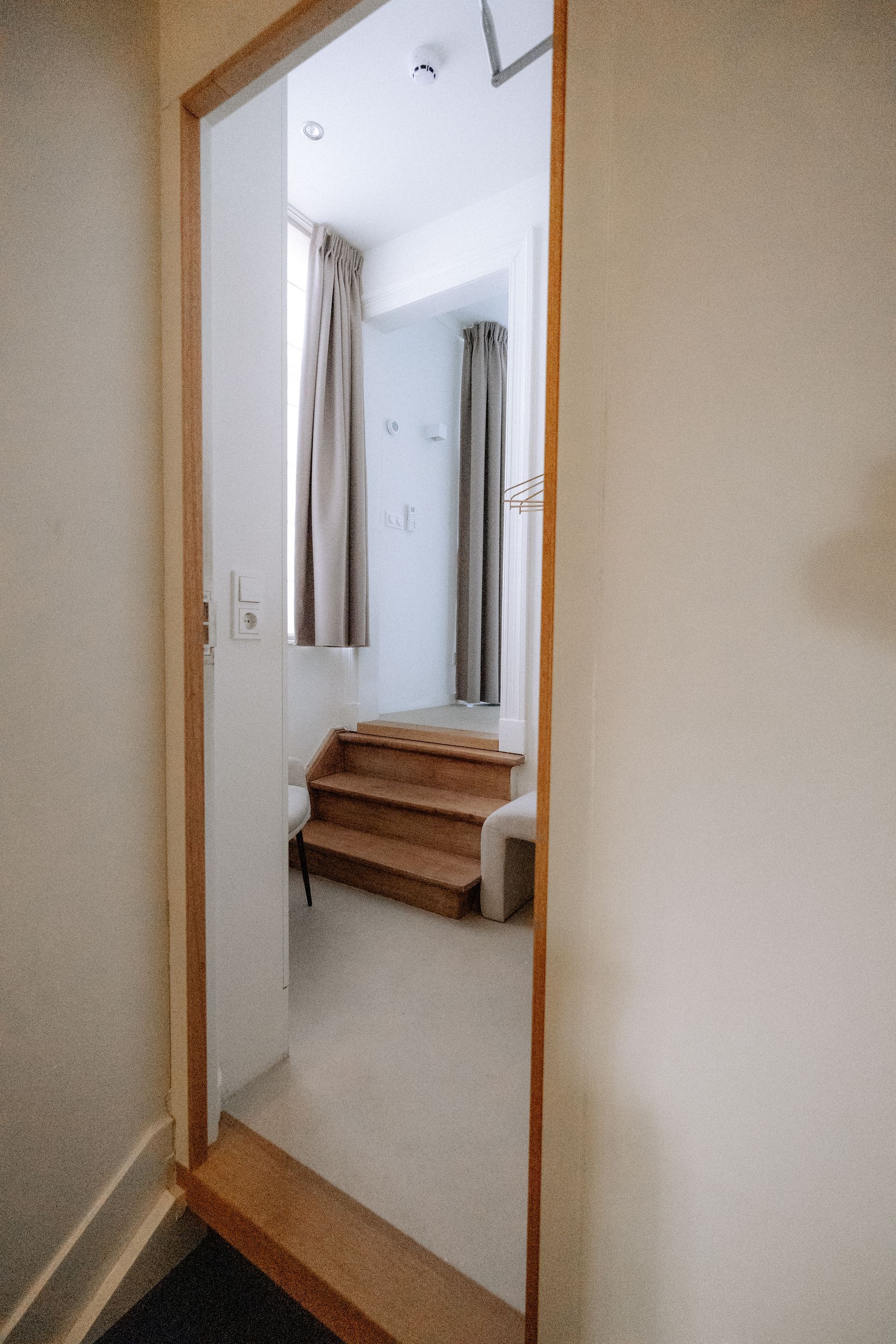 Haldeur met licht houten kozijn, die toegang geeft tot een ruimte met een kleine trap en gordijnen.