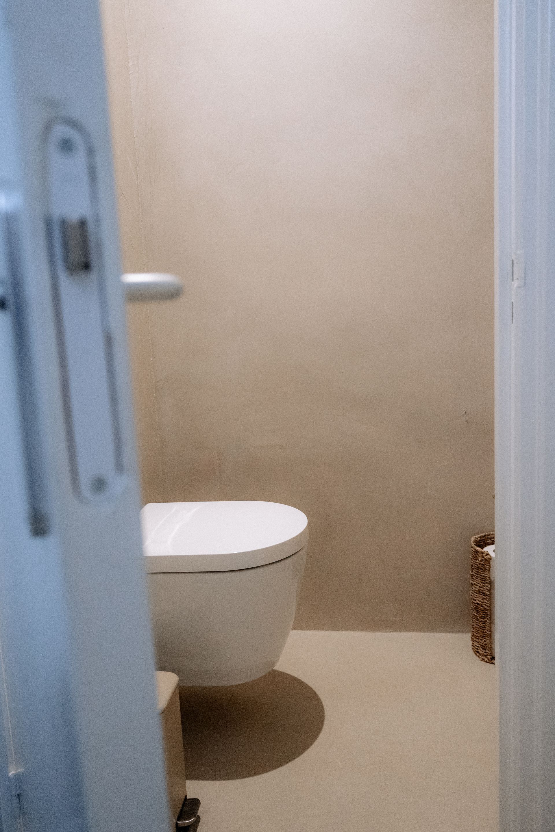 Toilet in een kleine badkamer met beige muren en vloer, zichtbaar door een gedeeltelijk openstaande deur.
