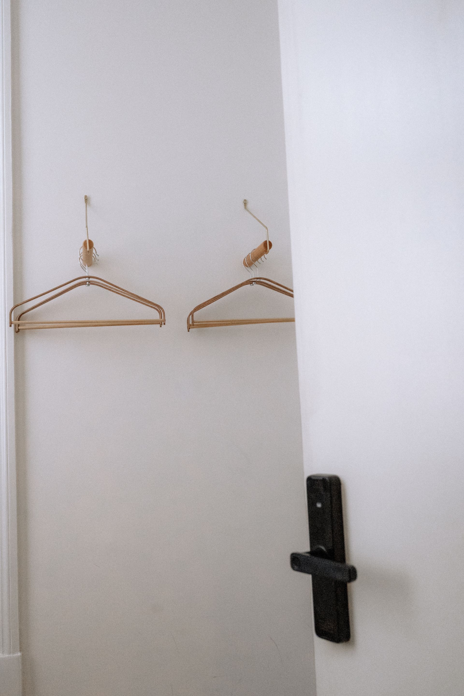 Twee messing kledinghangers aan een witte muur. Een witte deur met een zwarte klink staat gedeeltelijk open.