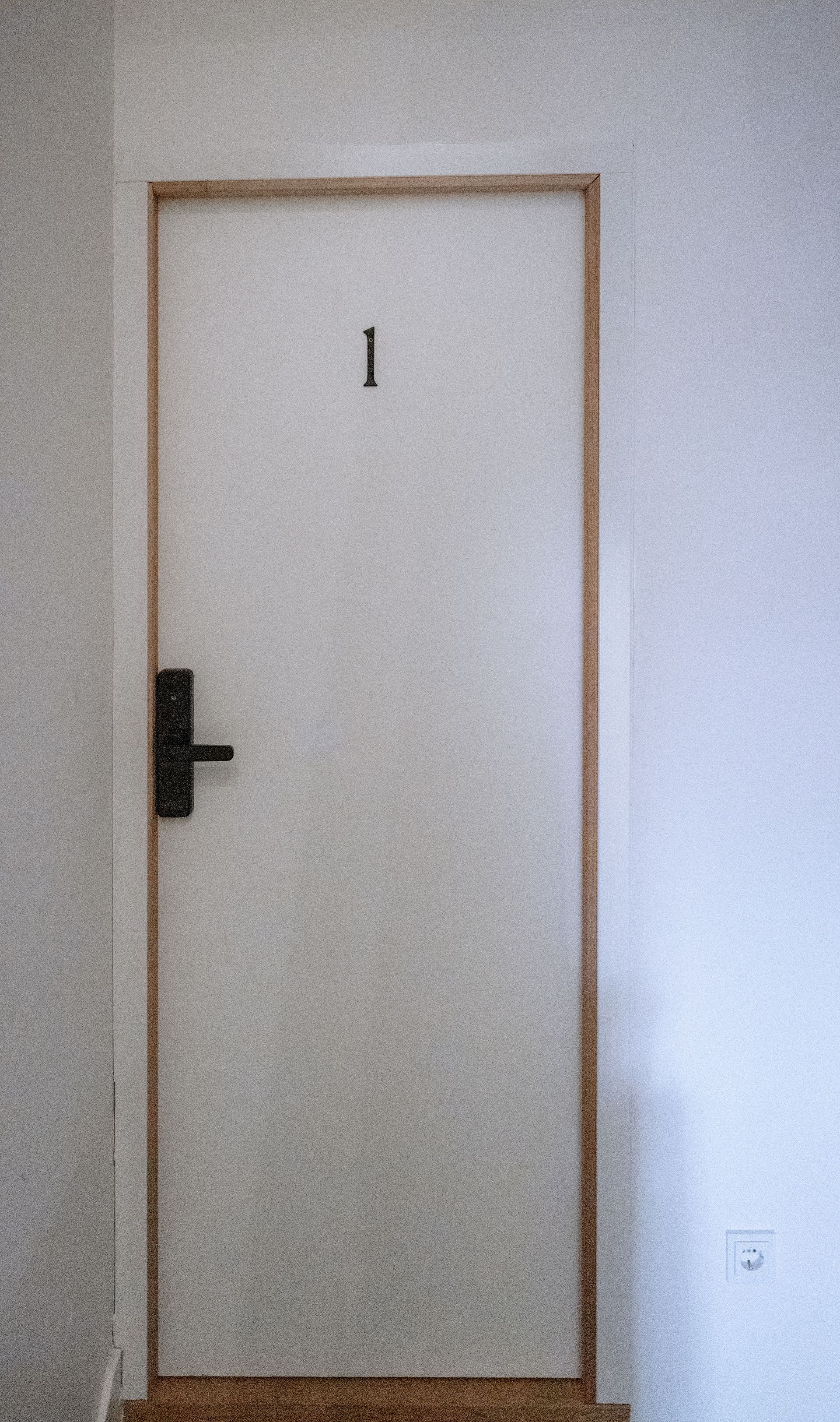 Witte deur met houten omlijsting en een zwarte handgreep, gemerkt met nummer 1.