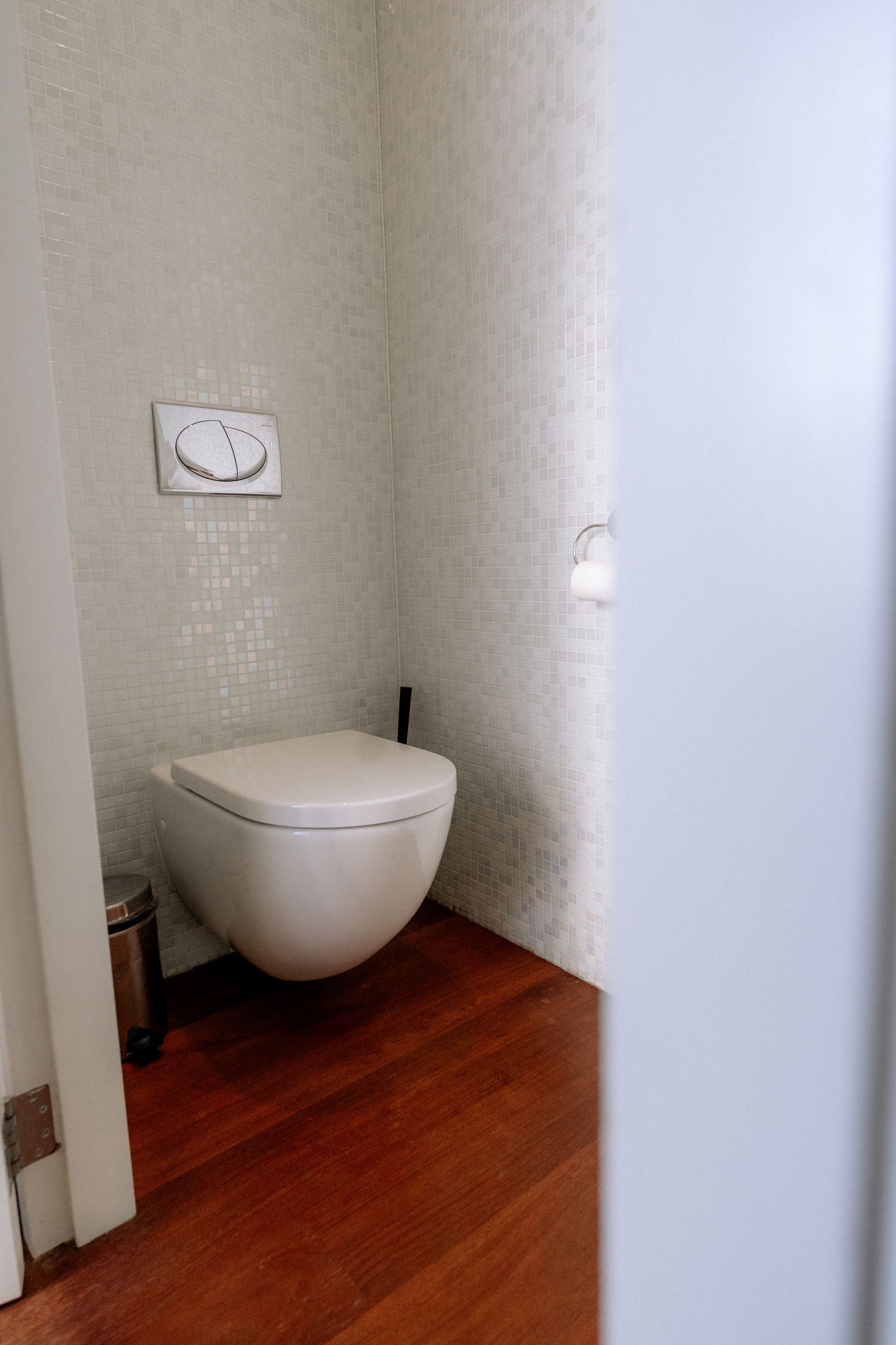 Wit toilet in een kleine badkamer met houten vloer en lichte, gestructureerde muren.