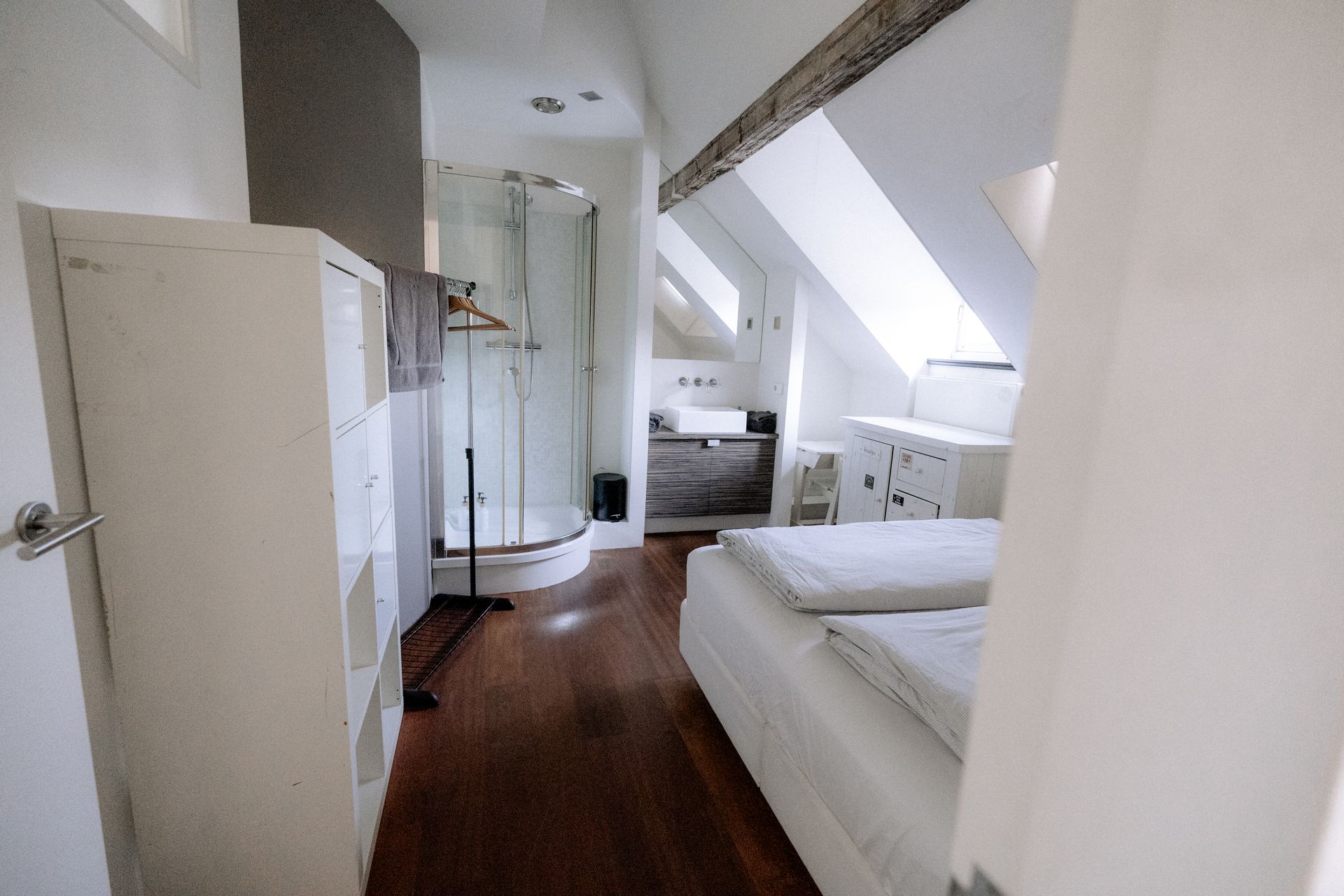 Slaapkamer met houten vloer, witte muren, bed, douche, kast en raam.