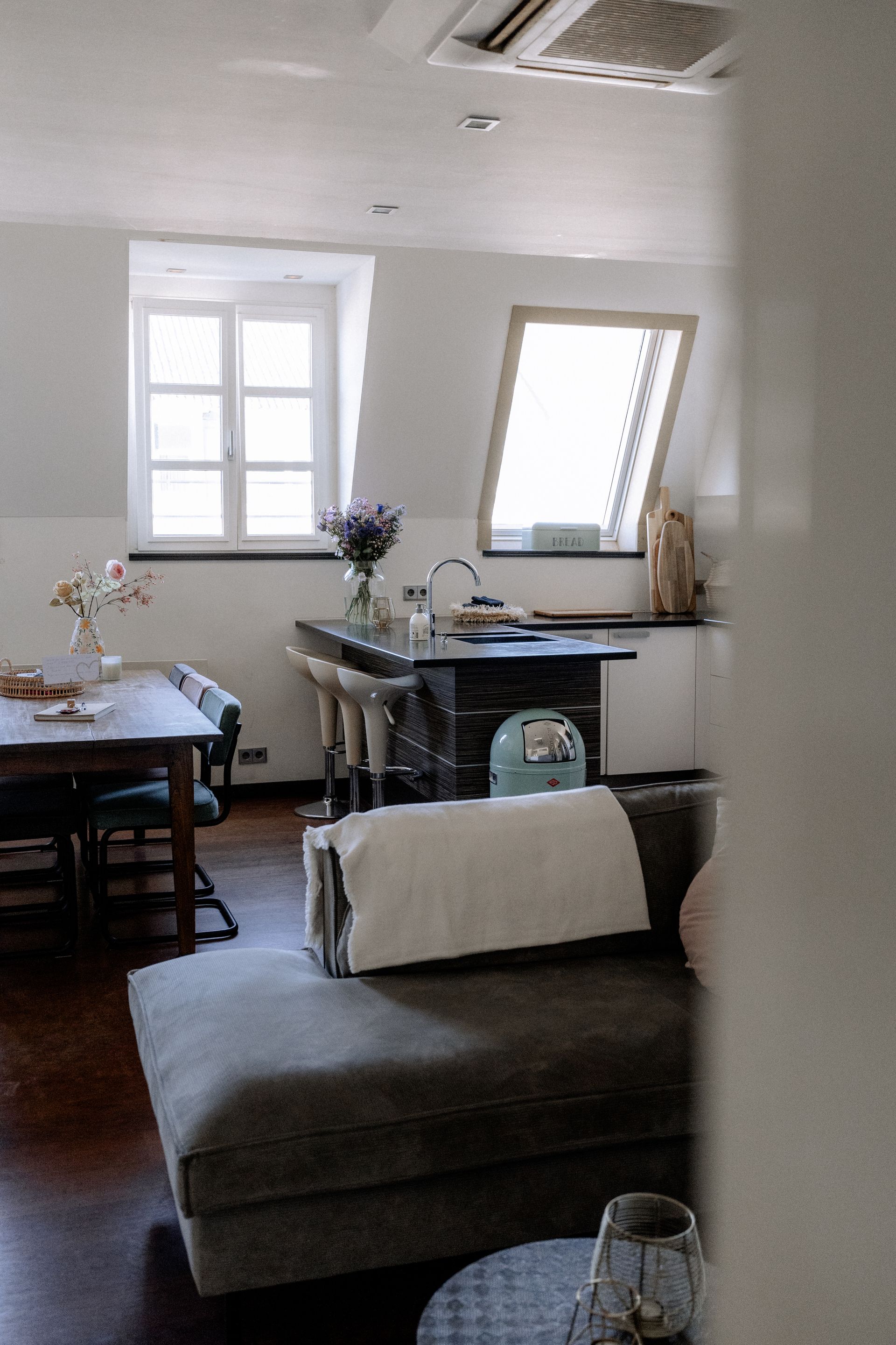 Gezellig interieur: kookeiland, eettafel, grijze chaise longue en een raam.