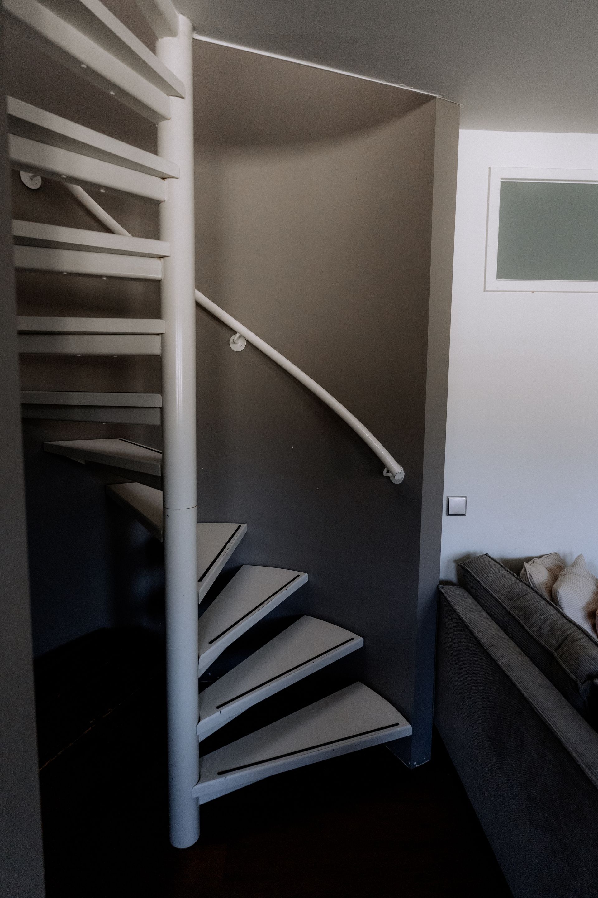 Witte wenteltrap naast een grijze muur en leuning, binnen.