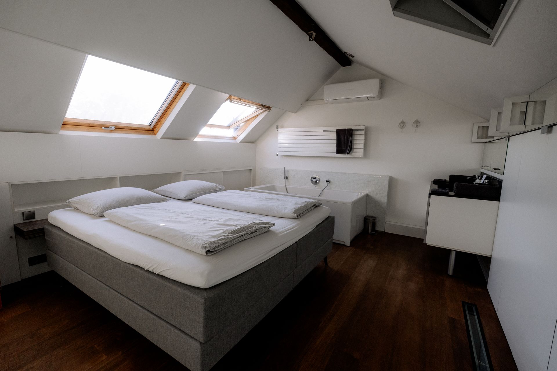 Slaapkamer met bed, dakramen en donkere houten vloer.